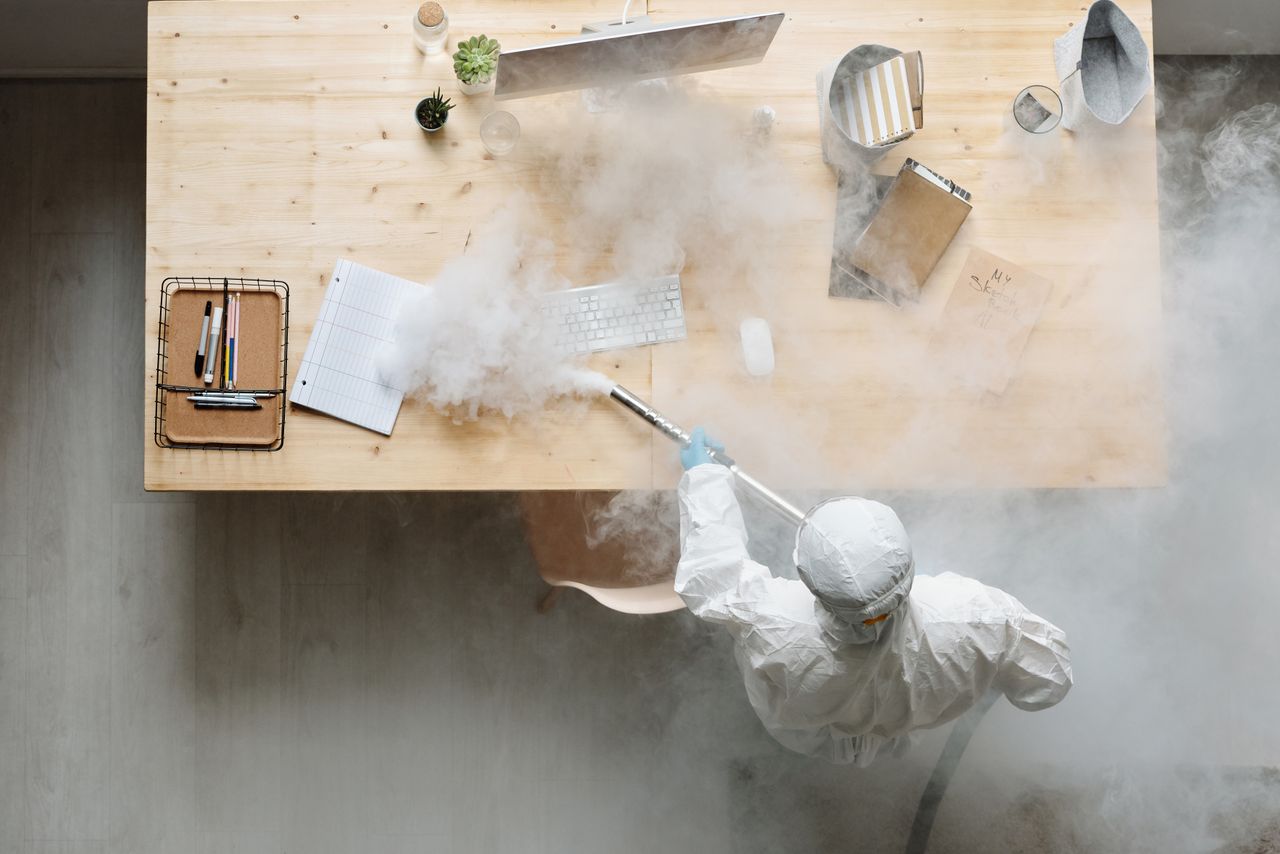 services-05 An individual disinfects a workspace using fumigation, wearing full protective gear for safety.
